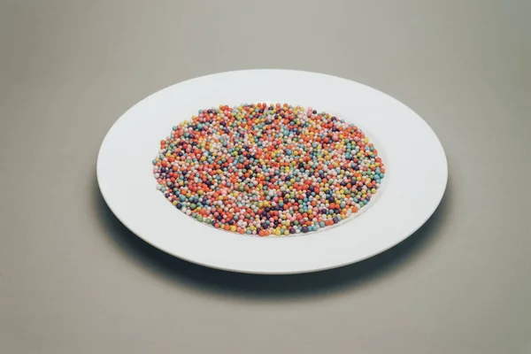 White plate with color preparations (vitamins, dyes, flavor enhancers, nutritional supplements, innovative technologies, candy sweets) on a gray background.