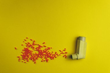 Yellow asthma inhaler with particle aerosol spay made by red preparations (vitamins, dyes, flavor enhancers, nutritional supplements, innovative technologies, candy sweets)  on a yellow background. 
