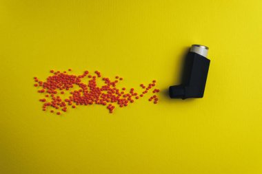 Kırmızı preparatlar (vitaminler, boyalar, lezzet arttırıcılar, besin takviyeleri, yenilikçi teknolojiler, şeker tatlılar) sarı bir arka plan tarafından yapılan parçacık aerosol spay ile siyah astım inhaler. 