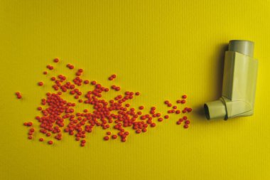 Yellow asthma inhaler with particle aerosol spay made by red preparations (vitamins, dyes, flavor enhancers, nutritional supplements, innovative technologies, candy sweets)  on a yellow background. 