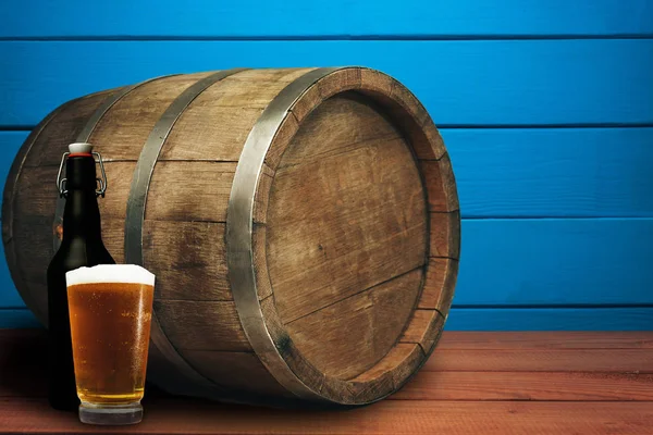Wooden barrel, glass of beer and black bottle on a red wood table wood. Beautiful  blue wooden background.