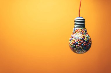 Yaratıcı ampul arkasında turuncu bir arka plan üzerinde çok renkli topu ile dolu. En iyi fikir konsepti.