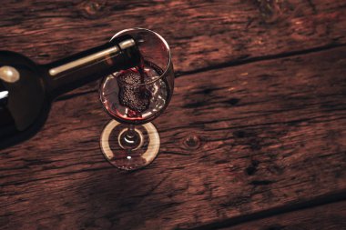 Eski ahşap bir masaya kırmızı şarap şişesi ve bir kadeh şarap dökmek. 