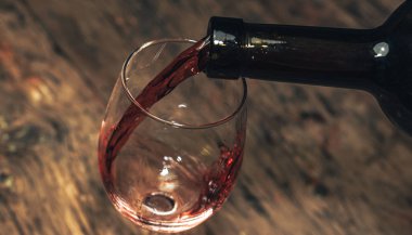 Eski ahşap bir masaya kırmızı şarap şişesi ve bir kadeh şarap dökmek. 