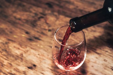 Eski ahşap bir masaya kırmızı şarap şişesi ve bir kadeh şarap dökmek. 