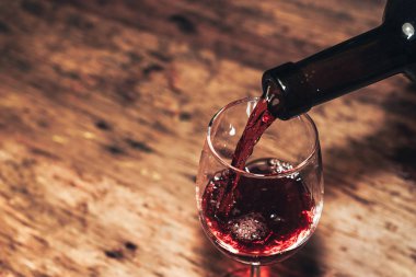 Eski ahşap bir masaya kırmızı şarap şişesi ve bir kadeh şarap dökmek. 