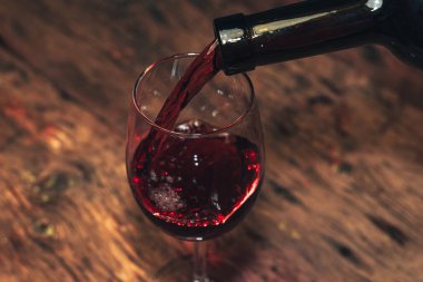 Eski ahşap bir masaya kırmızı şarap şişesi ve bir kadeh şarap dökmek. 