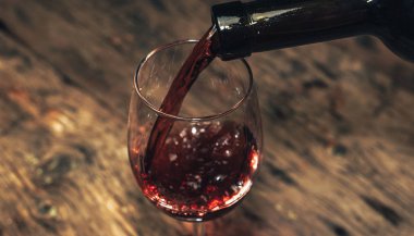 Eski ahşap bir masaya kırmızı şarap şişesi ve bir kadeh şarap dökmek. 