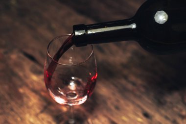 Eski ahşap bir masaya kırmızı şarap şişesi ve bir kadeh şarap dökmek. 