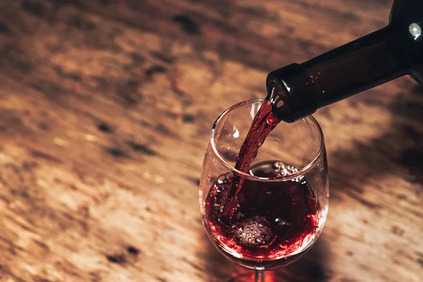 Eski ahşap bir masaya kırmızı şarap şişesi ve bir kadeh şarap dökmek. 