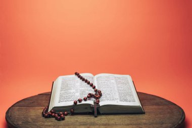 İncil ve haç boncukları eski yuvarlak masada. Güzel mercan turuncu arka plan. Din kavramı.