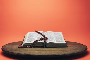 İncil ve haç boncukları eski yuvarlak masada. Güzel mercan turuncu arka plan. Din kavramı.