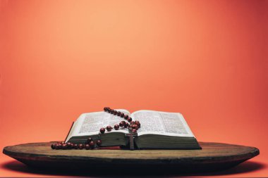 İncil ve haç boncukları eski yuvarlak masada. Güzel mercan turuncu arka plan. Din kavramı.