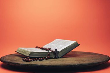İncil ve haç boncukları eski yuvarlak masada. Güzel mercan turuncu arka plan. Din kavramı.