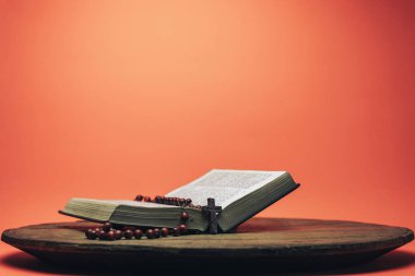 İncil ve haç boncukları eski yuvarlak masada. Güzel mercan turuncu arka plan. Din kavramı.