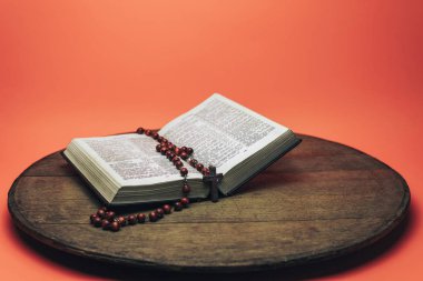 İncil ve haç boncukları eski yuvarlak masada. Güzel mercan turuncu arka plan. Din kavramı.