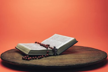 İncil ve haç boncukları eski yuvarlak masada. Güzel mercan turuncu arka plan. Din kavramı.