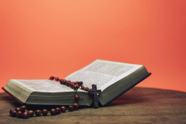 İncil ve haç boncukları eski yuvarlak masada. Güzel mercan turuncu arka plan. Din kavramı.