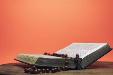 İncil ve haç boncukları eski yuvarlak masada. Güzel mercan turuncu arka plan. Din kavramı.