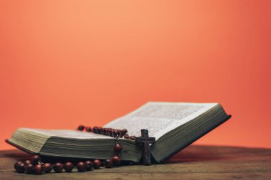 İncil ve haç boncukları eski yuvarlak masada. Güzel mercan turuncu arka plan. Din kavramı.