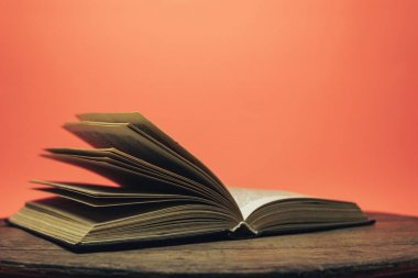 Eski bir ahşap yuvarlak masa üzerinde açık kitap. güzel mercan turuncu arka plan.