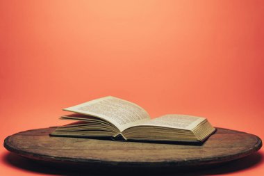 Eski bir ahşap yuvarlak masa üzerinde açık kitap. güzel mercan turuncu arka plan.