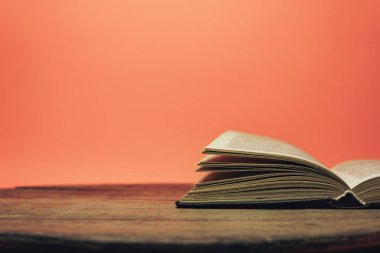 Eski bir ahşap yuvarlak masa üzerinde açık kitap. güzel mercan turuncu arka plan.