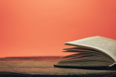 Eski bir ahşap yuvarlak masa üzerinde açık kitap. güzel mercan turuncu arka plan.