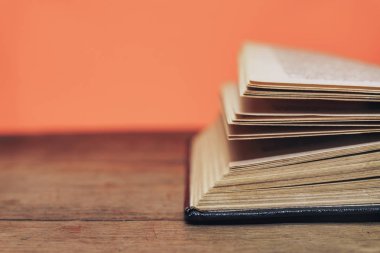 Eski bir ahşap yuvarlak masa üzerinde açık kitap. güzel mercan turuncu arka plan. Yakın çekim.