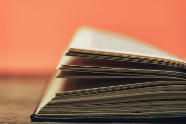 Eski bir ahşap yuvarlak masa üzerinde açık kitap. güzel mercan turuncu arka plan. Yakın çekim.