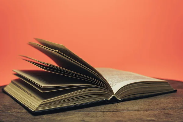 Open book on a  old wooden round table. beautiful coral orange background.