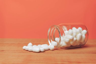 Kırmızı ahşap bir masada haplar için cam şişe. Güzel corall turuncu arka plan. 