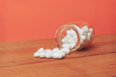 Kırmızı ahşap bir masada haplar için cam şişe. Güzel corall turuncu arka plan. 