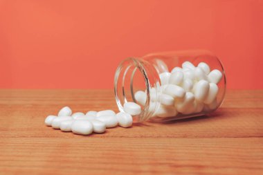 Kırmızı ahşap bir masada haplar için cam şişe. Güzel corall turuncu arka plan. 