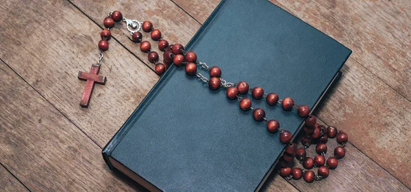 Old red Beads and crucifix on a Holy Bible background.