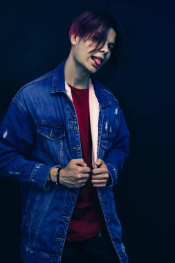 Koyu mavi arka planda, kırmızı gömlekli, pembe ve siyah saçlı genç bir adam..