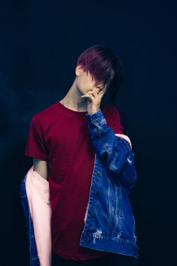 Koyu mavi arka planda, kırmızı gömlekli, pembe ve siyah saçlı genç bir adam..