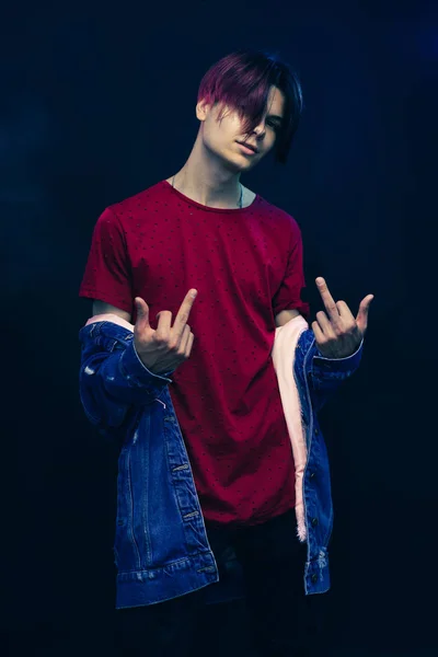 Young man with pink and black hair in red shirt on a dark blue background.