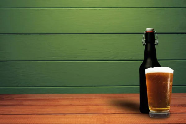 Glass of beer and black bottle beer on a red wood table wood. Beautiful  green wood background.
