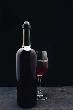 Koyu ahşap bir masa siyah arka plan behaid üzerinde kırmızı şarap ve şarap kadehi Şişe.