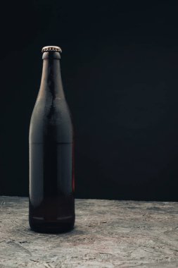Koyu ahşap bir masa ve siyah arka plan behaid üzerinde cam kahverengi şişe bira.