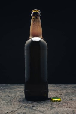 Koyu ahşap bir masa ve siyah arka plan behaid üzerinde cam kahverengi şişe bira.
