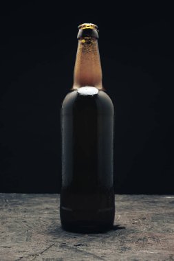 Koyu ahşap bir masa ve siyah arka plan behaid üzerinde cam kahverengi şişe bira.