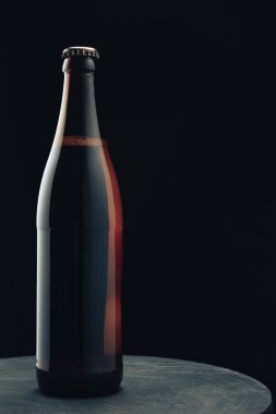 Koyu yuvarlak ahşap masa ve siyah arka plan behaid üzerinde Cam kahverengi şişe bira.