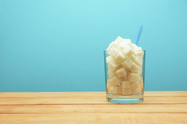 Cam küpler şeker dolu bir ahşap masa güzel mavi arka plan üzerinde saman-sağlıksız diyet kavramı.