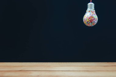 Yaratıcı ampul arkasında siyah arka plan ve kırmızı ahşap zemin veya masa aşağı çok renkli top ile dolu. En iyi fikir konsepti.