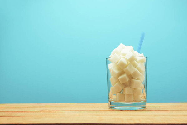 Стакан полный кубиков сахара с соломой на деревянном столе красивый синий фон - нездоровая концепция диеты
.