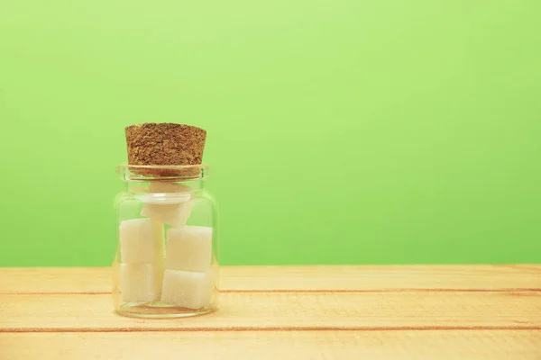 小玻璃瓶充满了立方体糖在木桌上美丽的绿色背景 不健康的饮食概念 — 图库照片