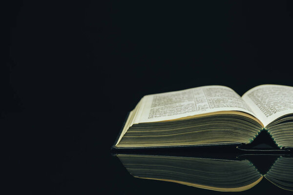 Open Holy Bible on a black glass table dark background