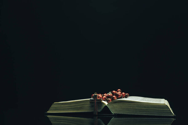 Open Holy Bible and beads on a black glass table dark background